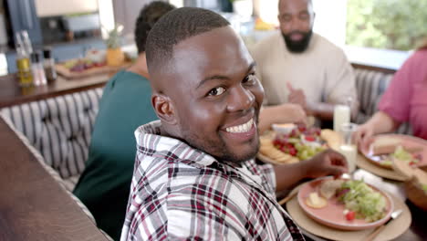 smiling man enjoying meal with diverse friends at home, sharing food and laughter