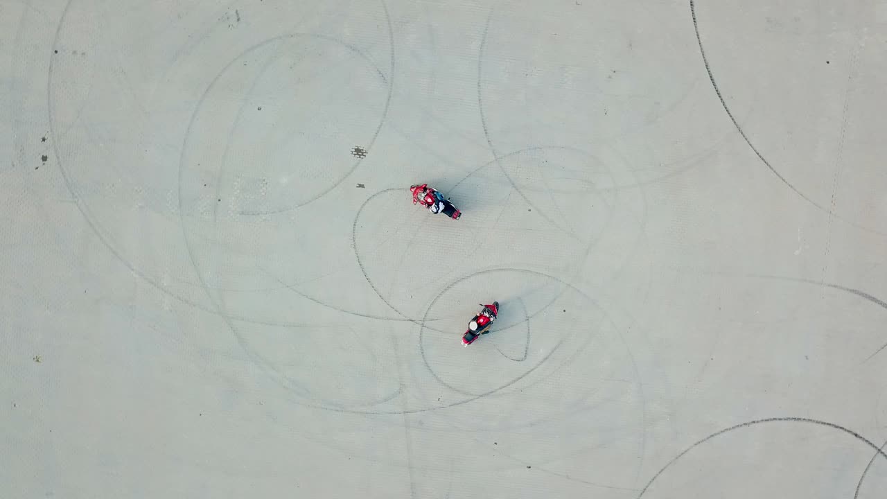 Aerial view of two red motorbikes racing high speed on a road in a circle way. Drivers on their motorcycles training on a race track outdoors. Camera moves around in a circle.