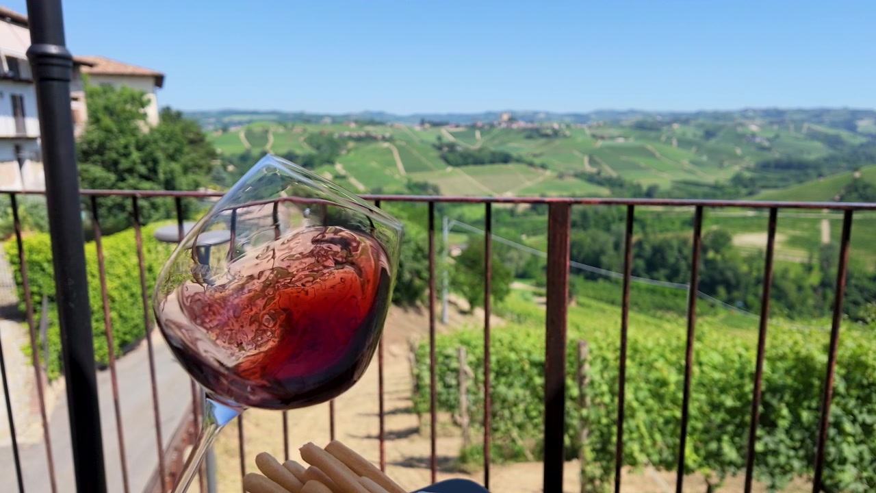 Gros plan au ralenti de vin rouge tourbillonnant dans un verre, avec en arrière-plan des collines de vignobles vallonnées.