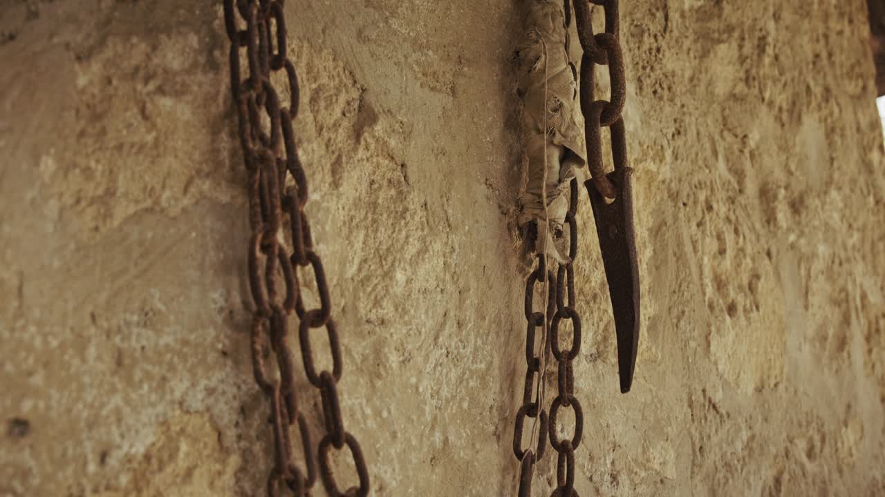 Rusty chains hanging against an old stone wall, showcasing aged metal textures
