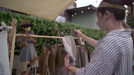 asian woman wearing face mask browsing selection of naturally hand made cotton clothing