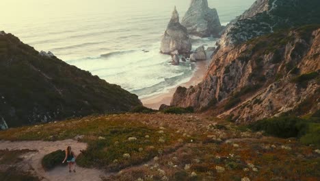 Girl-running-down-a-cliff-towards-Ursa-Beach,-Sintra,-Portugal