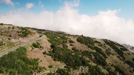 Antena-De-Carretera-Escénica-De-Montaña,-Nubes-Bajas,-Coche-En-Movimiento,-Dron-Soleado-De-Madeira