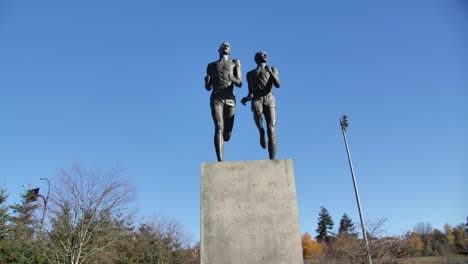 two statues of runners mid-stride on a pedestal, blue sky background in vancouver