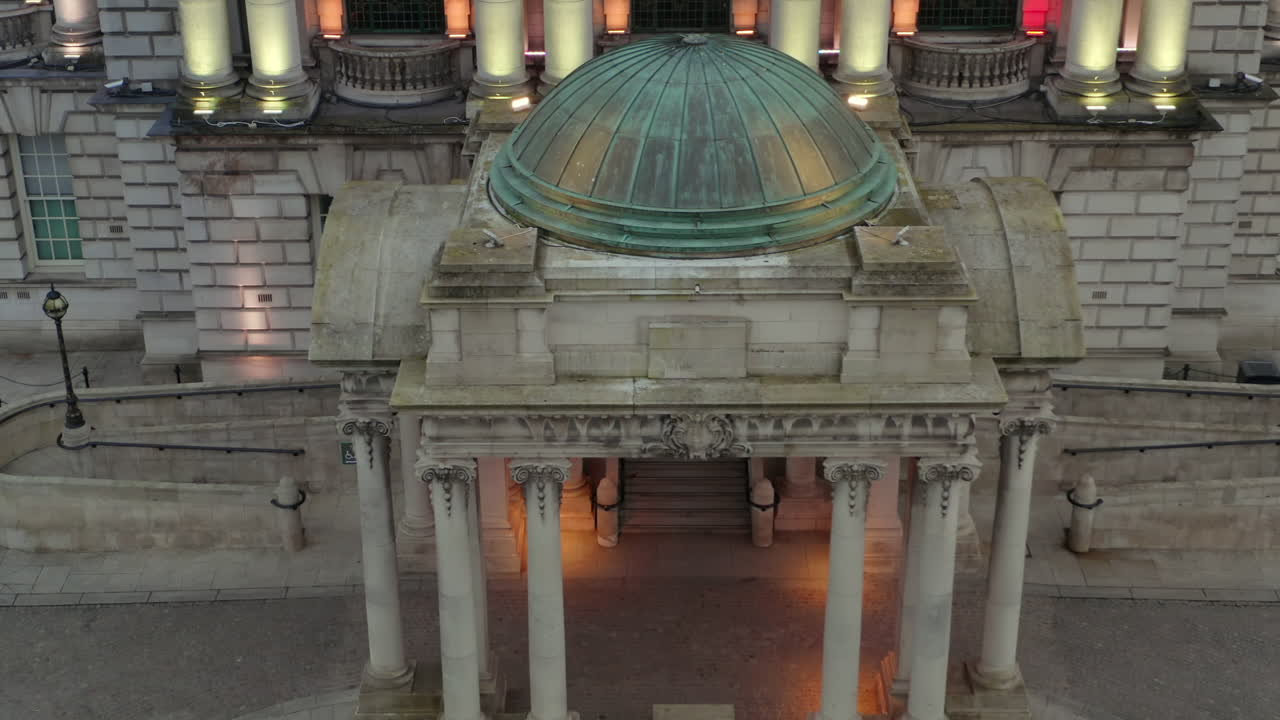 Aerial pan of Belfast City Hall's main portico featuring illuminated columns and copper dome
