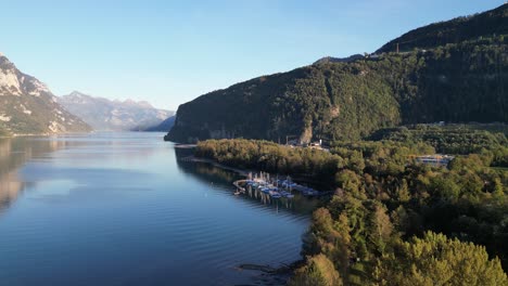 A-sunny-view-of-Lake-Walensee-with-crystal-blue-water,-a-small-harbor,-and-a-mountain-backdrop-on-a-beautiful-day