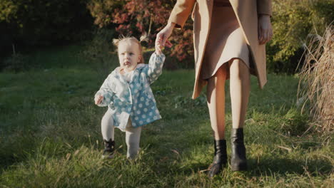 Mom-leads-the-hand-of-a-little-girl,-walking-in-the-park