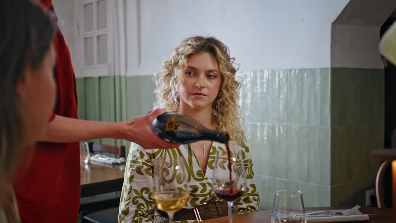 Close de duas amigas sendo garçonetes e servindo vinho em taças em um restaurante