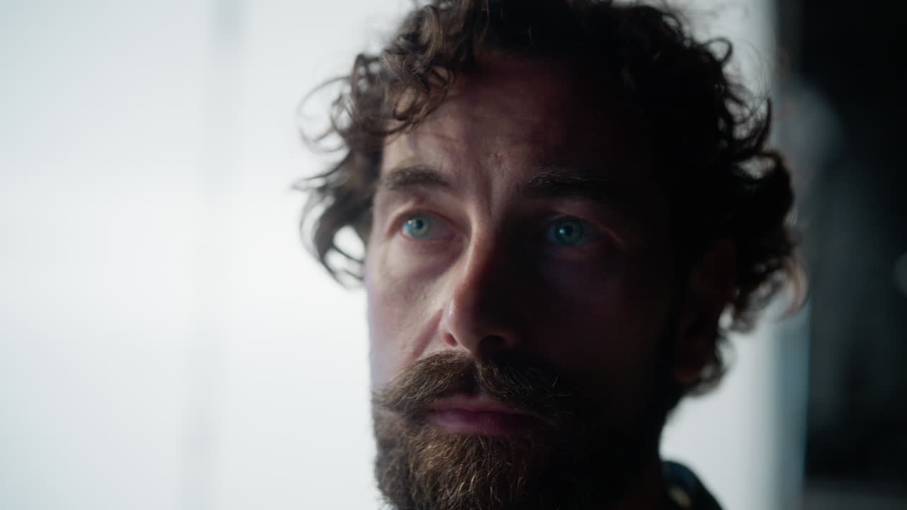 Close-up portrait of a man with blue eyes and a beard, partially in shadow