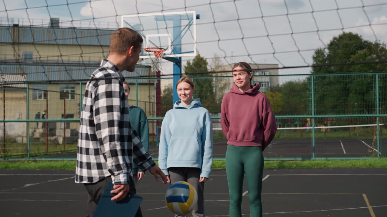 волейболисты практикуют свои навыки с тренером на открытом поле, стоя уверенно и улыбаясь, тренировка проходит под чистым небом, в окружении деревьев и жилых зданий