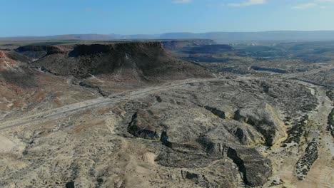 aerial view moves away shot, scenic view of highway in the middle of rocky and the desert landscape in of la purisima baja california sur, mexico, mountain range in the background