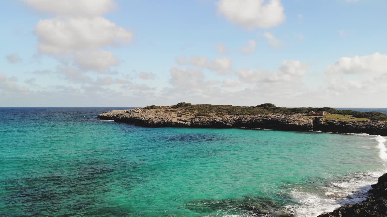 Ripresa aerea con drone di una costa rocciosa in netto contrasto con l'acqua blu brillante del Mediterraneo che si infrange sulle rocce di Maiorca