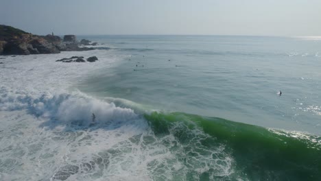 Aerial-view-of-surfers-enjoying-riding-Punta-Zicatela-shimmering-sunlit-blue-sea-waves,-Oaxaca,-Mexico