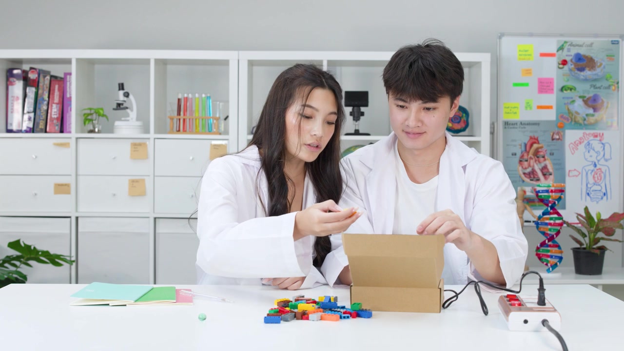 白衣を着た2人の学生が、おもちゃのブロックと電子機器を使ってSTEMプロジェクトで協力している。