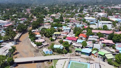 Drone-Aéreo-De-La-Ciudad-Capital-Dili-Después-De-Un-Ciclón-De-Desastre-Natural-E-Inundaciones-Repentinas-En-Timor-Leste,-Sudeste-De-Asia,-Bajando-Sobre-Edificios,-Río-Y-Campo-De-Fútbol