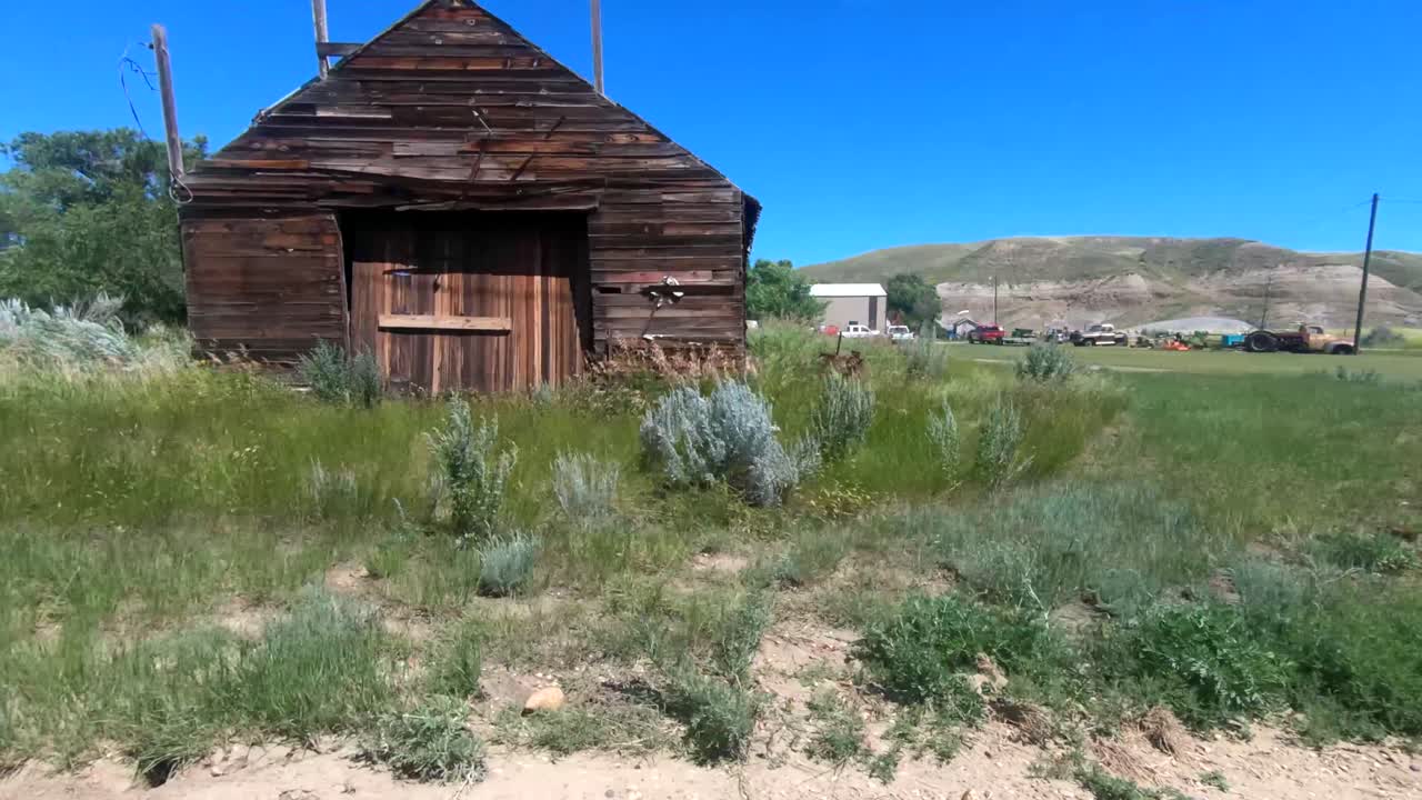 Driving by a farm with old vintage farming equipment in a field next to a old barn on a sunny day