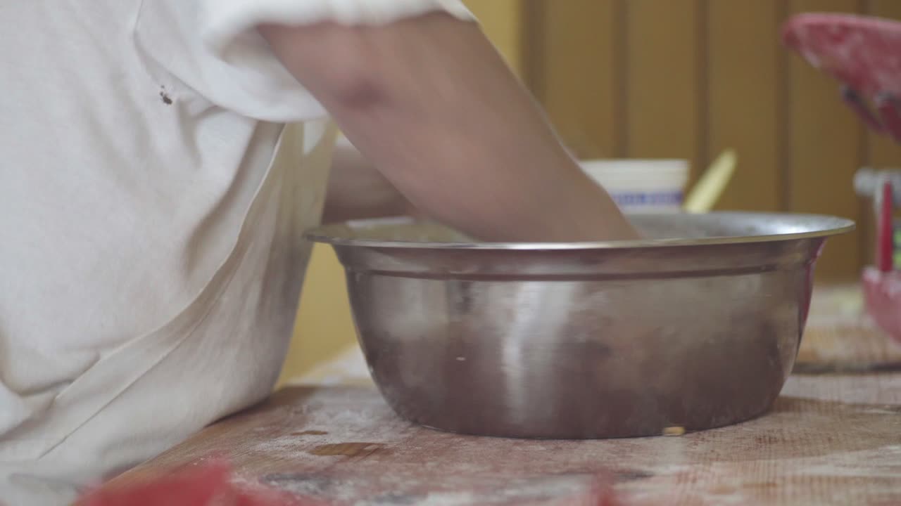 primer plano de un chef de pastelería mezclando vigorosamente la masa en un gran cuenco de metal para hornear