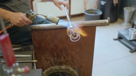 glassmith heats glassware with flame torch in workshop