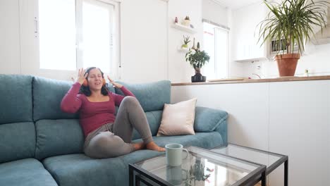 happy woman listening to music with her headphones and dancing while sitting on the couch