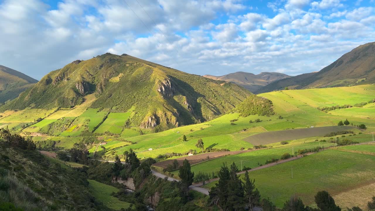 Ripresa a mano di un vasto paesaggio montano verde nelle Ande dell'Ecuador, con dolci colline, appezzamenti agricoli e un cielo azzurro nuvoloso