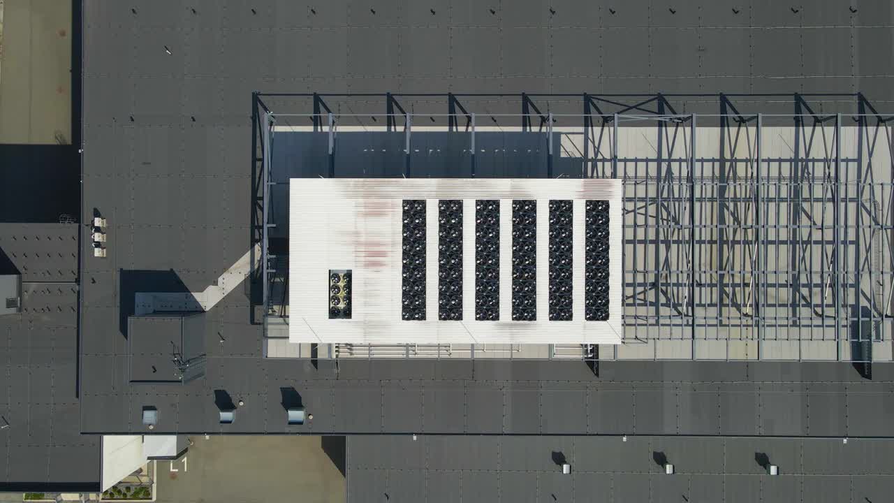 Droneoptagelse fra luften, set ovenfra, af køleventilatorer til datacenter eller serverrum monteret på et moderne arbejdspladstag på en solrig dag. Ventilatorer snurrer hurtigt og holder temperaturen kølig og lav.