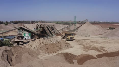 Ein-Großer,-Mit-Sand-Beladener-LKW-Fährt-Auf-Die-Baustelle-Zu,-Luftaufnahmen-Des-LKW-Neben-Der-Baustelle-Und-Materialien