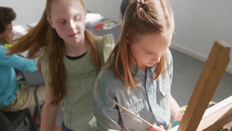 High-angle-video-of-two-caucasian-schoolgirls-in-art-class,-one-girl-admiring-the-other's-painting