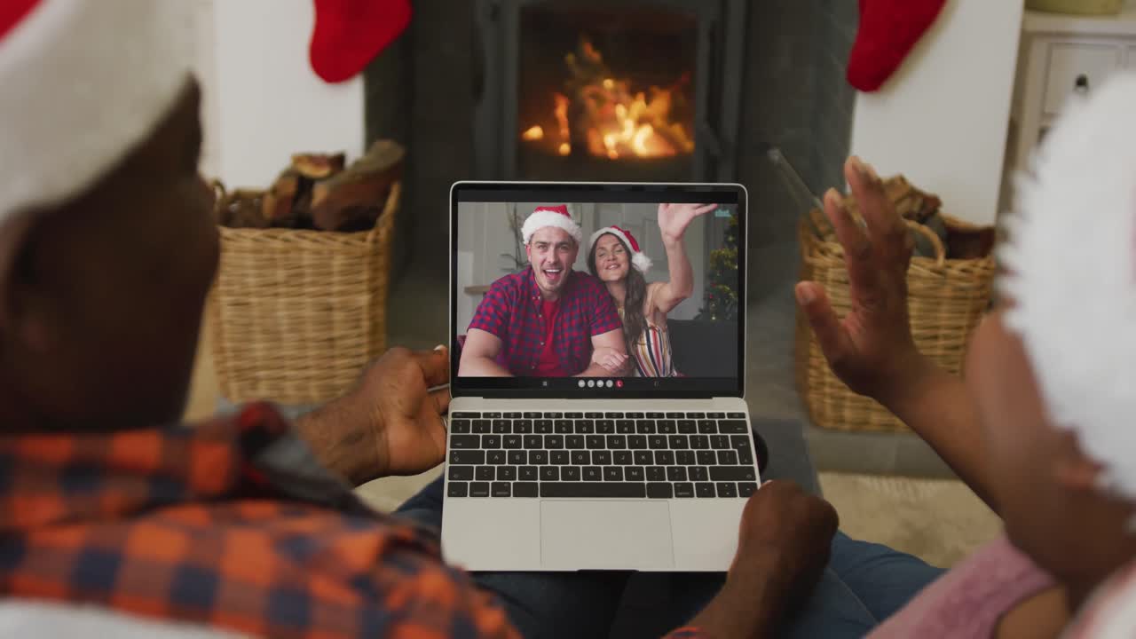 pareja afroamericana usando una computadora portátil para una videollamada de navidad con amigos sonrientes en la pantalla