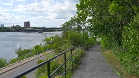 walking and biking trail with view to street and river below plus bridge and buildings in background under blue sky in summer in ottawa ontario canada