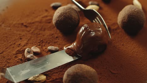 confectioner taking truffle candy covered by melted chocolate with iron spatula