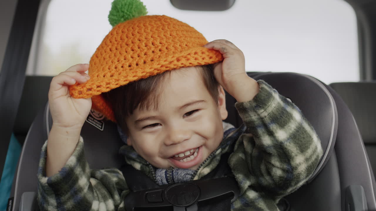 niño asiático feliz monta en un asiento de coche para niños, juega con un sombrero naranja, se divierte en un viaje