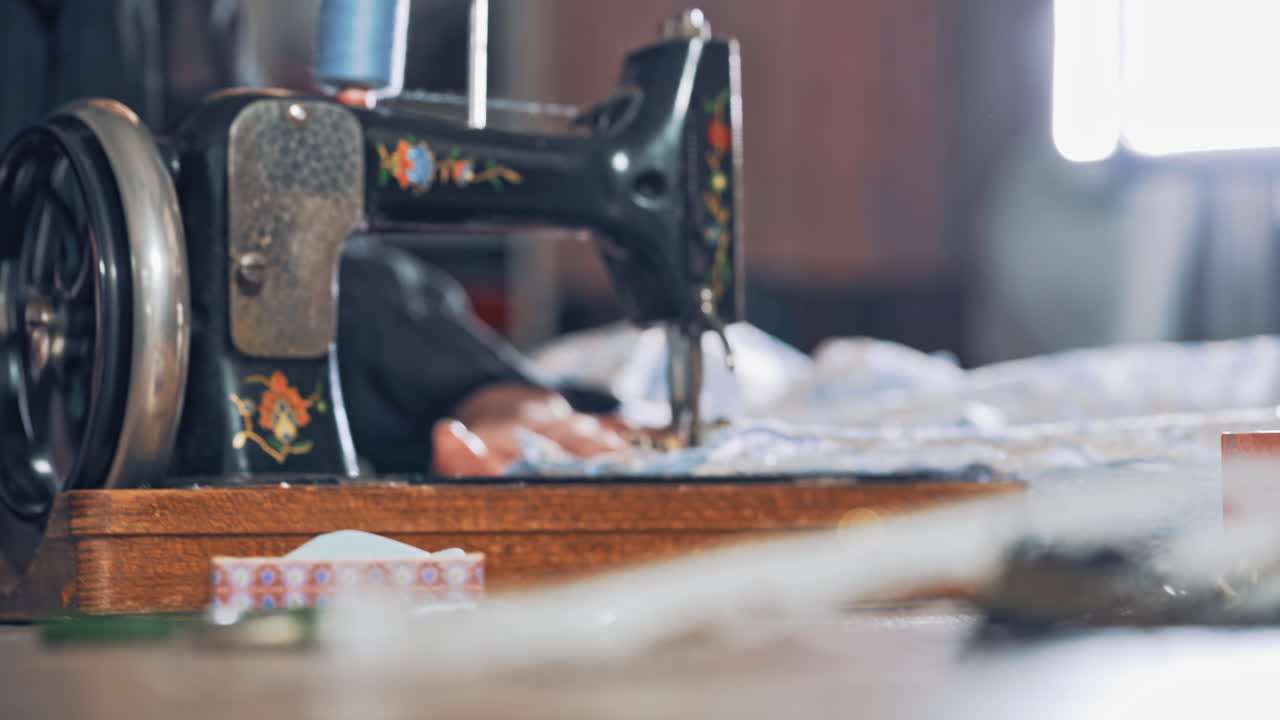 Female tailor works on a sewing machine at her workplace. Successful tailor sewing clothes in atelier with black sewing machine.