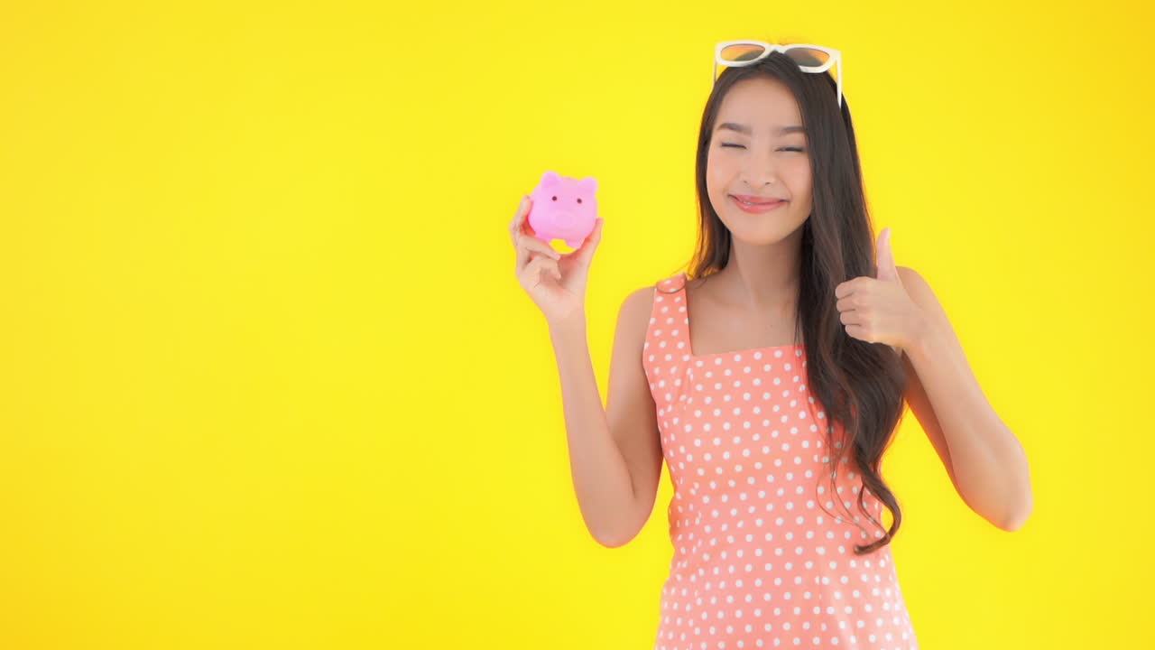 Young pretty woman in a sundress and sunglasses in front of a solid replaceable background raise a pink piggy bank up for display