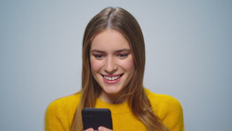 Retrato-De-Una-Mujer-Sorprendida-Leyendo-Buenas-Noticias-En-Un-Teléfono-Inteligente-Sobre-Fondo-Gris.