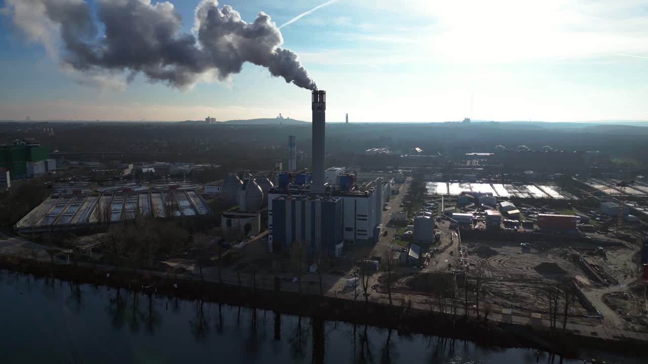 Waste to energy plant emitting smoke from its chimney, located near an urban area, environmental impact of waste. Stunning aerial view flight ascending drone