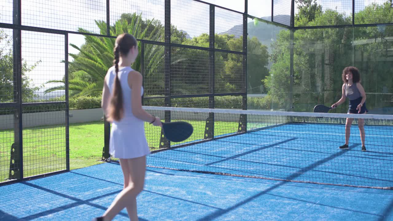 Diverse giocatrici che ricevono il servizio su un campo da padel blu, mentre giocano una partita informale e alzano le racchette.