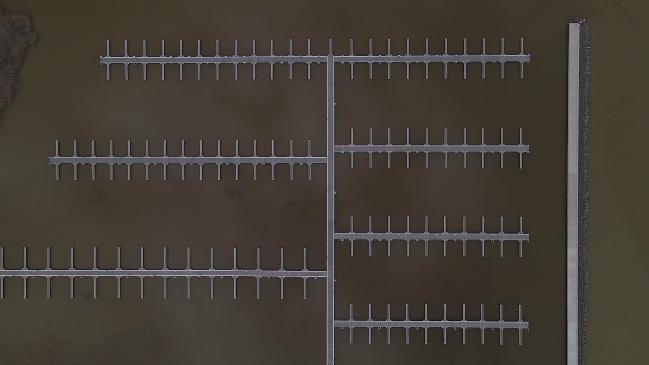 A symmetrical aerial view of empty floating docks extending into calm, dark water. The geometric pattern of the piers creates a visually striking and structured composition.