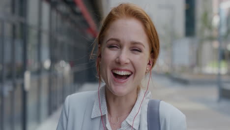 portrait happy young red head business woman laughing wearing earphones enjoying relaxed urban lifestyle listening to music in city slow motion