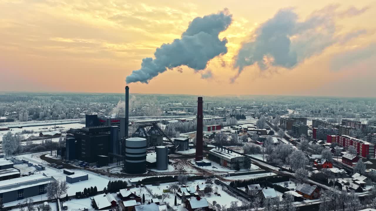 Vista aerea invernale di una centrale elettrica industriale con ciminiere che rilasciano vapore su una città innevata all'alba, che mette in evidenza la produzione di energia, l'inquinamento e le infrastrutture urbane