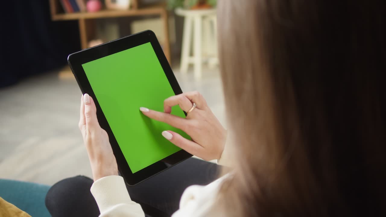 녹색 화면을 가진 가 태블릿을 사용하는 여성. 인식할 수 없는 여성이 크로마 키를 스와이프하고, 거실의 소파에 앉아 있습니다. 온라인 쇼핑, 인터넷 서핑. 집에서 여가 시간, 레저