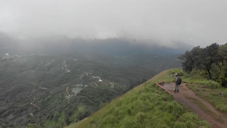 4k-Aerial-Reveal-Shot-of-a-25-year-old-Indian-Male-Standing-and-Shirui-Village-from-the-top-of-Shirui-Peak,-Ukurul,-Manipur,-India