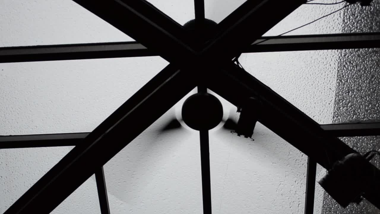 Il ventilatore sotto un soffitto di vetro. Gocce di pioggia cadono su un tetto.