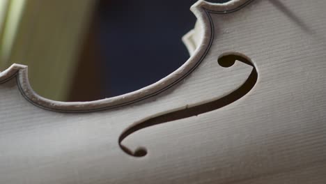 macro-close-up-of-artisan-luthier-maker-work-on-new-classic-handmade-raw-violin-smooth-edge-in-waist-and-purfling-rasp-in-workbench-of-workshop-in-Cremona-Italy-4k-video