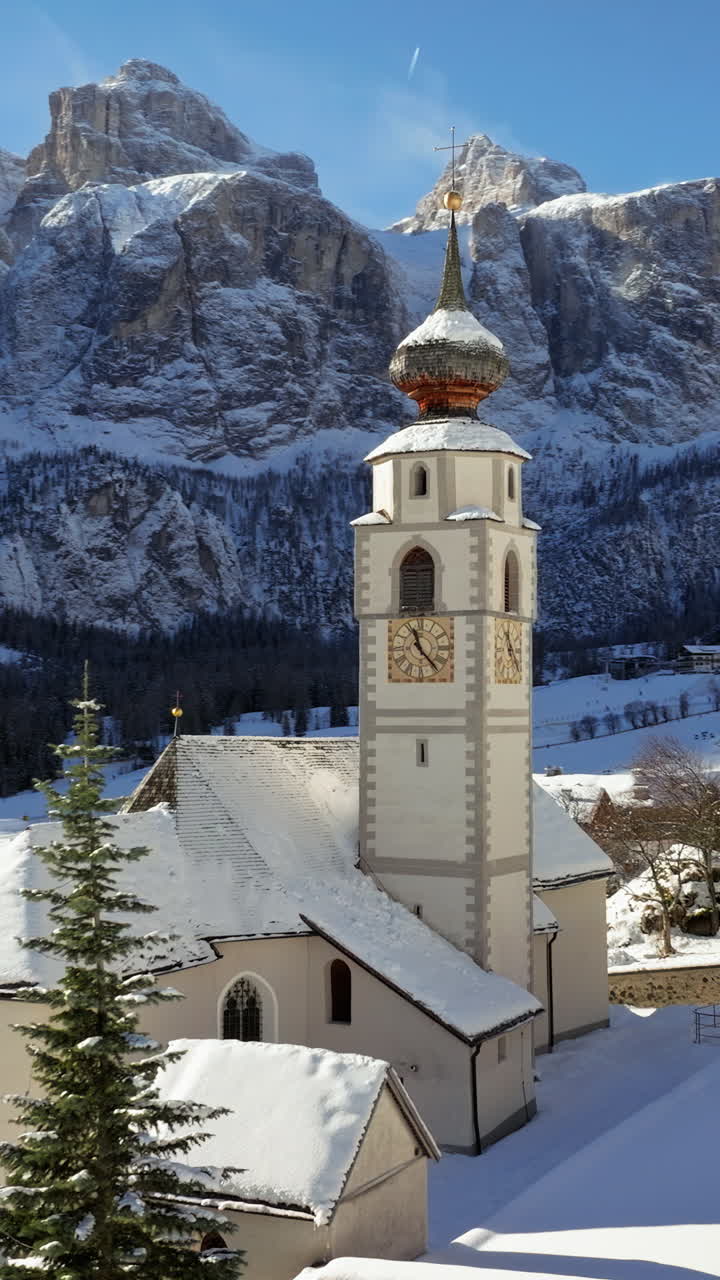 Aerial drone view of the Parrocchia di Colfosco in the Colfosco mountain village covered in snow, in South Tyrol, Dolomites, Northern Italy. Vertical