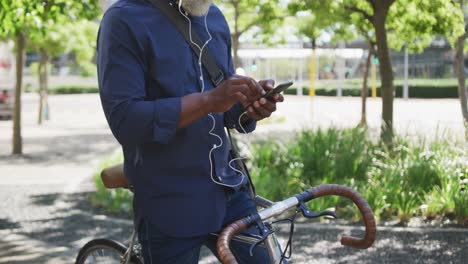 african american senior man using smartphone while sitting on bicycle on the road