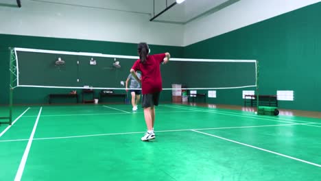 two women playing badminton in an indoor court