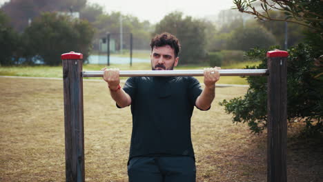 man trains with effort on the iron bar in the park