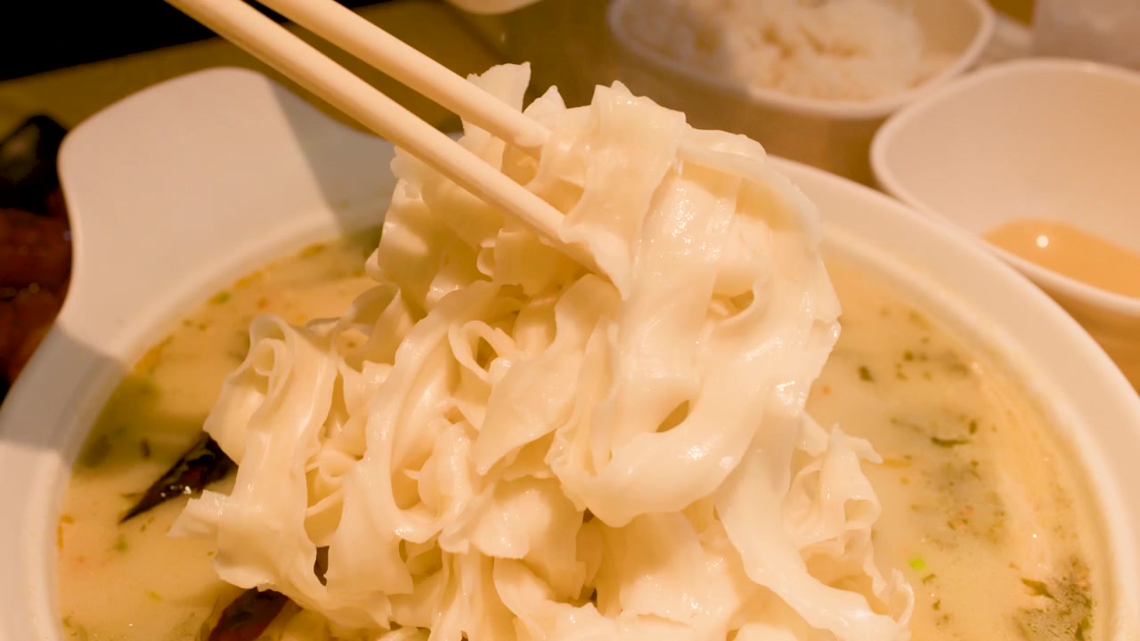 Primo piano di bacchette che sollevano noodles freschi da una ciotola di zuppa piccante