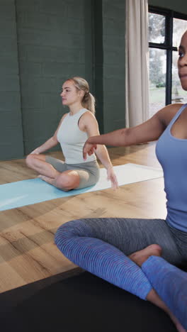 vertical video of focused diverse women meditating together on mats in yoga class, slow motion