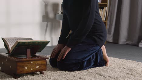 close up of muslim woman at home kneeling and reciting from the quran